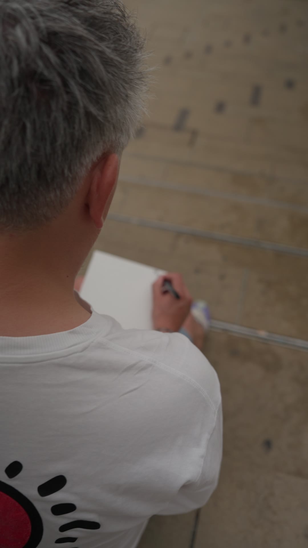 Melv dessine sur une toile posée sur ses genoux, assis sur les marches du quai