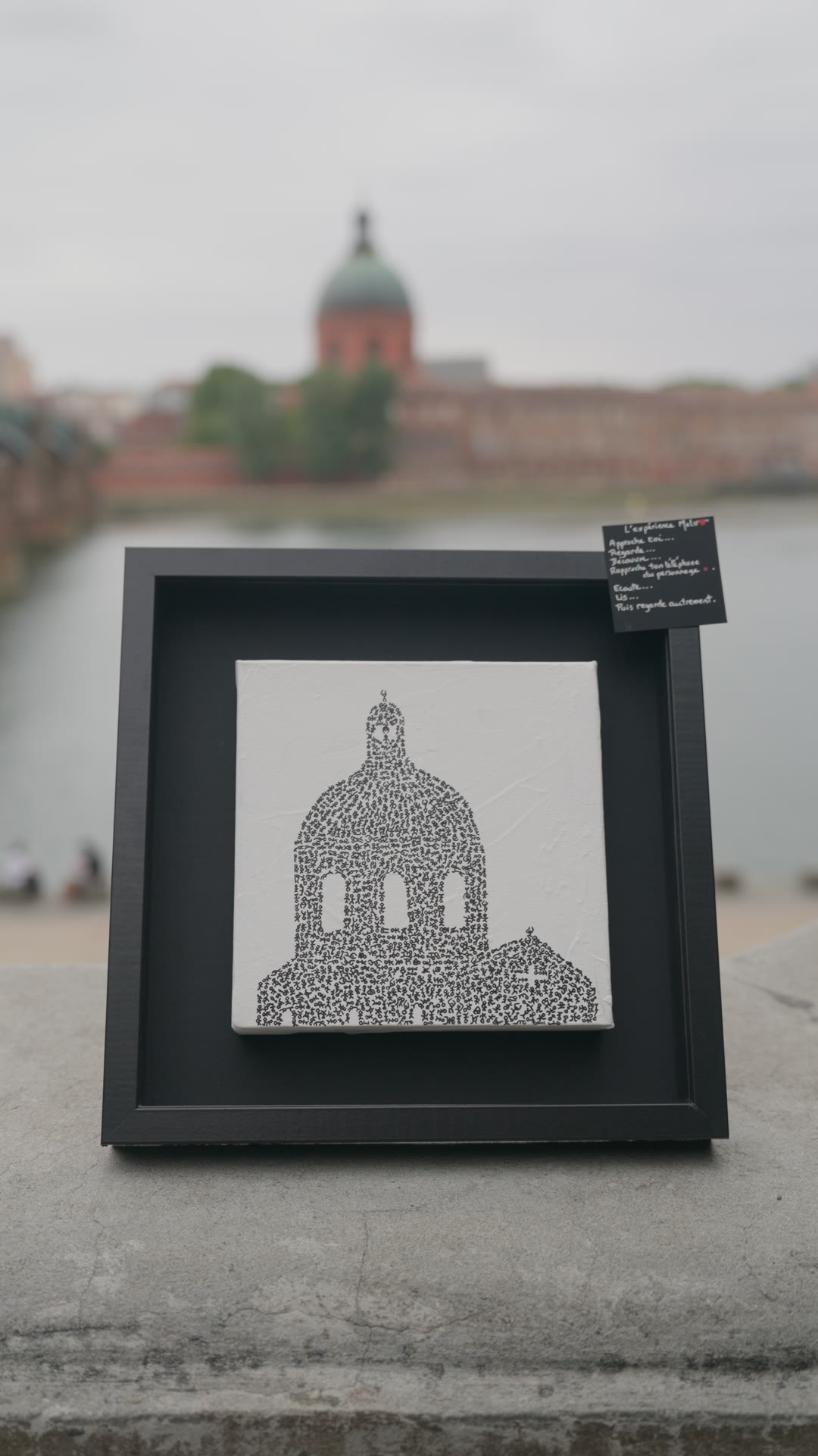 Le tableau encadré en noir sur le parapet, l'étiquette de l'œuvre accrochée au cadre